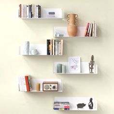 three white shelves with books, vases and other items on them against a wall