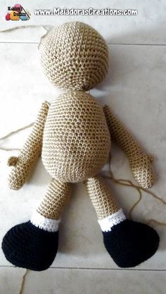 a crocheted teddy bear with black feet and white legs sitting on the floor