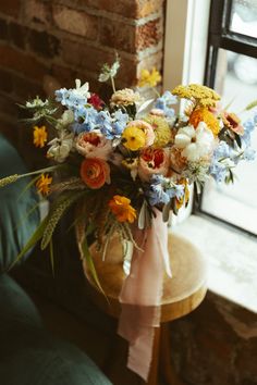 a vase filled with lots of colorful flowers on top of a wooden table next to a window