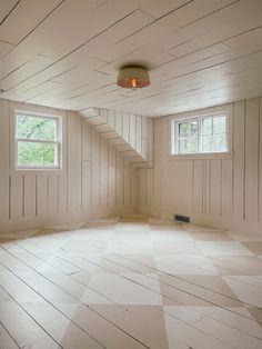 an empty room with white walls and wood flooring on the sides, two windows in the middle