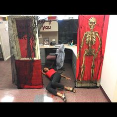 a woman laying on the floor in front of two halloween themed cubicle walls with skeleton decorations