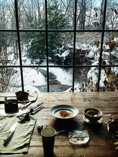 a wooden table topped with plates and bowls filled with food next to a large window