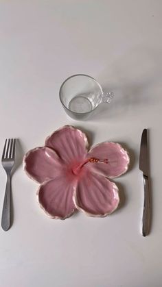 a pink flower sitting on top of a plate next to a knife and fork,