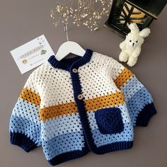 a crocheted sweater and teddy bear on a hanger next to a cardigan