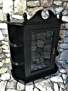 a small black cabinet sitting on top of a stone floor next to a brick wall