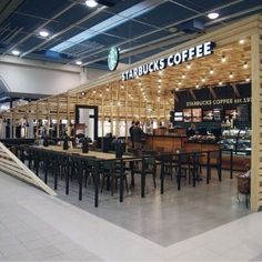 the inside of a starbucks coffee shop with tables and chairs in front of an escalator