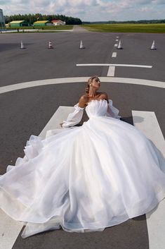 a woman in a white wedding dress sitting on the ground with her legs crossed and looking off to the side