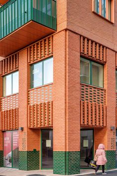 a woman walking down the street in front of a brick building with green balconies