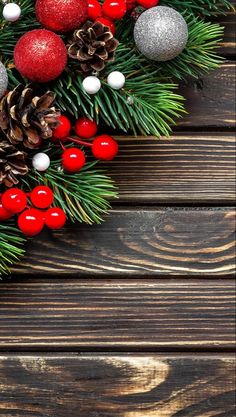 christmas decorations on wooden background with pine cones and red berries, fir - needles and silver baubles