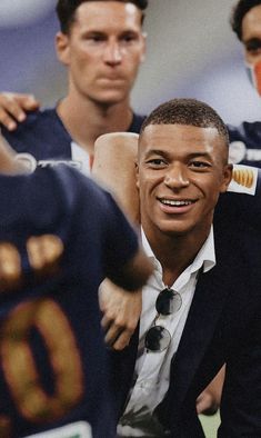 a man in a suit and tie standing next to two other men wearing sports uniforms