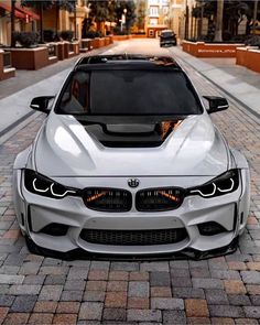 the front end of a white car parked on a brick road