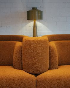 an orange couch sitting in front of a lamp on top of a wooden floor next to a white brick wall