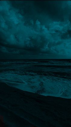 the sky is dark and cloudy over the water at night time, with waves coming in to shore