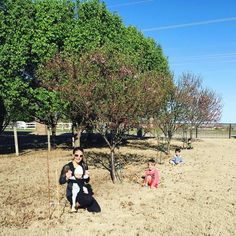 a woman and two children are sitting in the dirt near a tree with no leaves on it