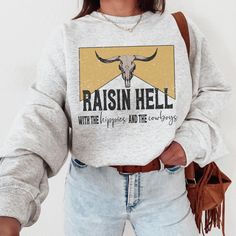 Wear this Raisin Hell With The Hippies and The Cowboys country western crewneck sweatshirt  to your next country concert or night out. This western graphic tee is slightly distressed and oversized, providing you with trendy style and comfort for that concert outfit with cowgirl aesthetic.  * Ultra soft * Distressed design * Pre-shrunk * Universal fit * True to size * DTG Printing * Brand - Gildan Refunds/Exchanges: * No Cancellations * No returns/exchanges * All sales are final Sizing: Our graphic tees and sweatshirts are a true to size standard unisex fit. For an oversized look, please size up. For a TShirt dress fit, we recommend sizing up at least two sizes. Please oversee the sizing chart provided in the listing photos to ensure your measurements are correct as we DO NOT offer cancella Fall Letter Print T-shirt For Country Concerts, Rodeo Crew Neck Top With Screen Print, Crew Neck Top With Screen Print For Rodeo, Rodeo Screen Print Crew Neck Top, Pre-shrunk Tops For Rodeo In Fall, Fall Letter Print Tops For Country Concerts, Letter Print Tops For Country Concerts In Fall, Fall Crew Neck Band Merch Top, Fall T-shirt With Letter Print For Country Concerts