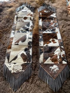 two brown and white cow hide rugs on top of a sheepskin area with fringe trim