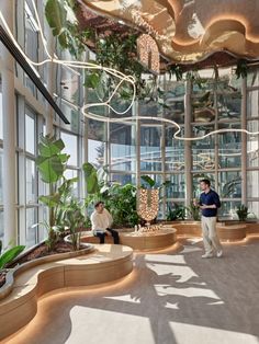 two people are sitting in the middle of a room filled with plants and potted plants