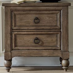 an old wooden nightstand with two drawers and a clock on top, in front of a white wall