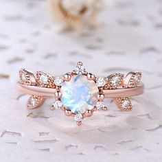 an opal and diamond ring on top of a white table with flowers in the background