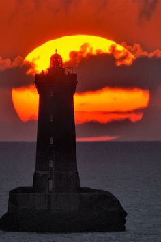 the sun is setting behind a lighthouse in the middle of the ocean with dark clouds