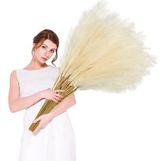 a woman in white holding a bunch of dry grass