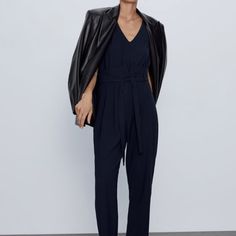 V-Neck Jumpsuit With Short Sleeves. Pleats At Waist And Tonal Belt. Back Hidden In Seam Closure With Opening And Button Casual V-neck Jumpsuits And Rompers For Work, Chic V-neck Business Casual Pantsuit, Black V-neck Jumpsuits And Rompers For Office, Office V-neck Black Jumpsuit, Black V-neck Jumpsuit For Office, Casual V-neck Pantsuit For Work, V-neck Jumpsuits And Rompers For Office In Spring, Chic Workwear Pantsuit With Tie Waist, Casual V-neck Pantsuit For Night Out