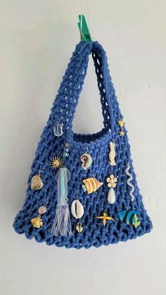 a blue crocheted purse hanging from a hook on a white wall with sea creatures and seashells all over it