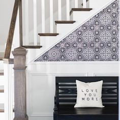 a black and white pillow sitting on top of a wooden bench under a stair case