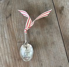 a spoon with a red and white striped ribbon on it sitting on top of a wooden table