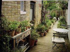 an outdoor patio with lots of potted plants on the table and chairs next to it