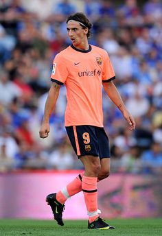 a soccer player in an orange shirt is on the field with his head turned to look down