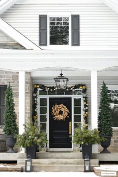 a front porch decorated for christmas with potted trees and wreaths on the door