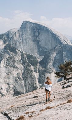 a woman running up the side of a mountain in front of a large rock formation