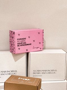 three boxes are stacked on top of each other in front of a white wall with pink lettering