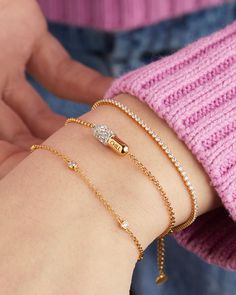 a woman's arm with three bracelets on it and a pink sweater in the background