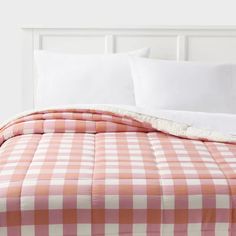 a bed with pink and white checkered comforter on it, next to pillows