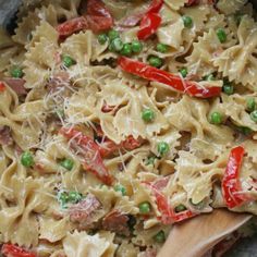 a pan filled with pasta and peas on top of a stove next to a wooden spoon