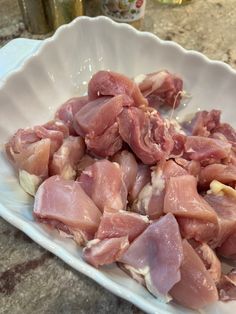 raw meat in a white bowl sitting on a counter top next to a glass bottle