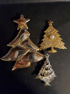 three christmas tree shaped brooches sitting on top of a black table next to each other