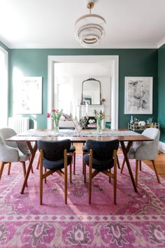 a dining room with green walls and pink rug on the floor, chairs around a wooden table