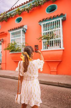 a woman in a white dress taking a photo with her cell phone on the street