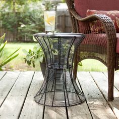 a wicker chair and table on a wooden deck in front of a garden area