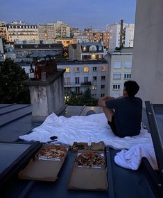 a man sitting on top of a roof next to two pizzas and some boxes