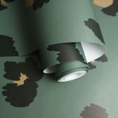 a green wallpaper with black and gold flowers on the wall next to a lamp