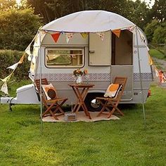 an rv is parked in the grass next to a table and chairs