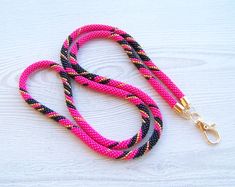 a pink and black dog leash with gold hardware on a white wooden surface next to a golden metal hook