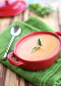 a red bowl filled with soup sitting on top of a green napkin next to a spoon