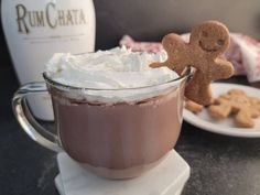 a cup of hot chocolate with whipped cream and a gingerbread man on the side