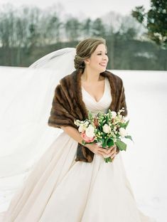 a woman in a wedding dress and fur stole holding a bouquet with flowers on it