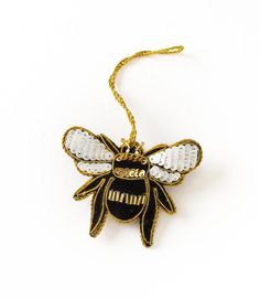 a black and white bee ornament hanging from a gold chain on a white background